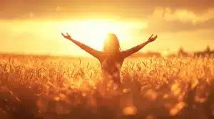 a happy woman raising her arms in a rural field during sunset, golden light illuminating her figure, soft background, ideal for themes of joy, praise, and connection with nature.