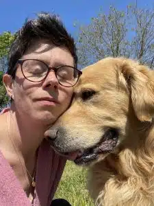 Céline Caille avec un chien dans un parc en plein air, soleil et ciel bleu.