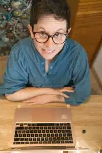 Personne souriante avec lunettes devant un ordinateur portable